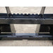 Close-up of black painted steel pallet fork attachment showing central mounting plate and weld reinforcements on gravel ground