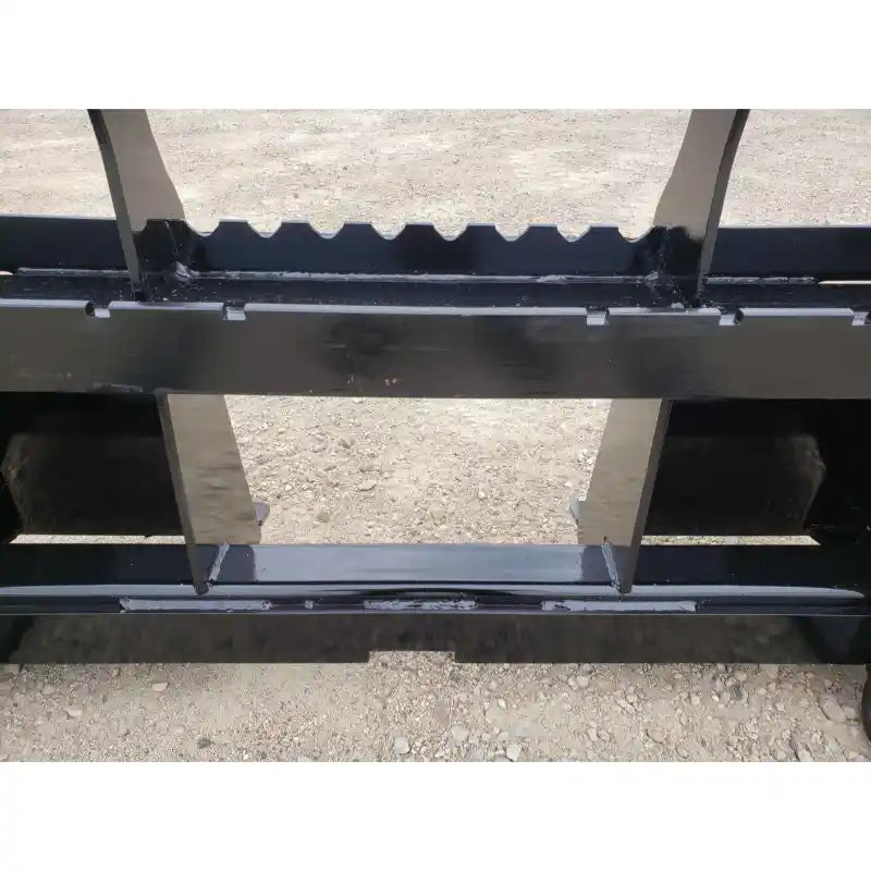 Close-up of black painted steel pallet fork attachment showing central mounting plate and weld reinforcements on gravel ground