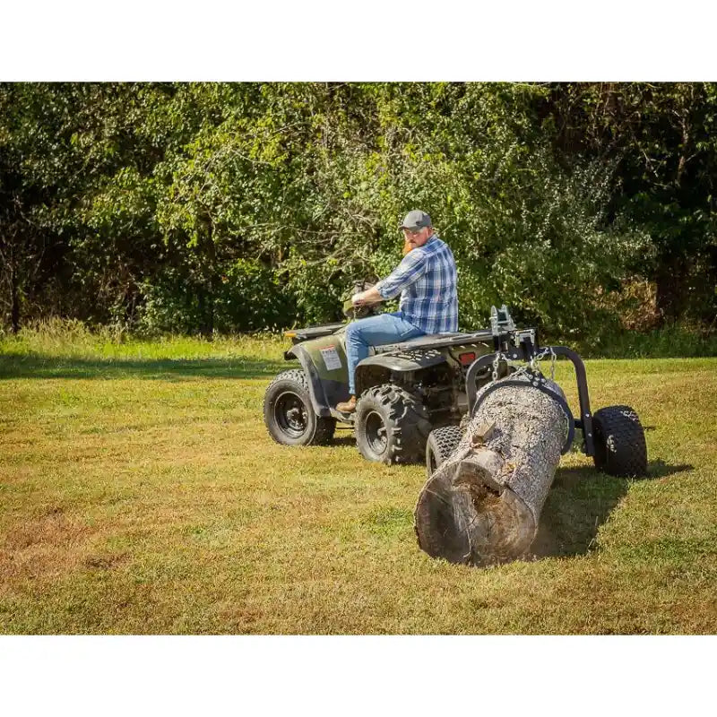 Rear view of operator on ATV using Swisher log skidder to haul large timber across grass, gallery position 1