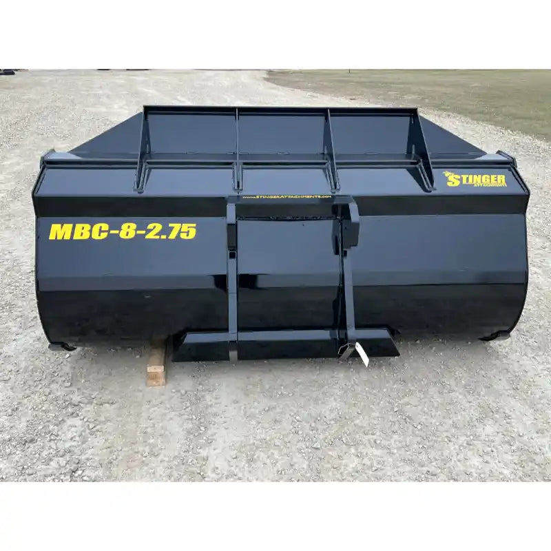 Front view of black steel construction material bucket attachment with yellow model markings on gravel surface