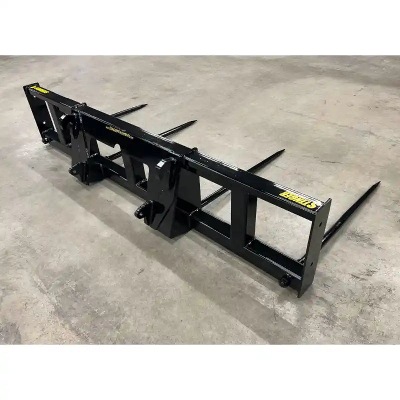 Black steel bale spear attachment with four pointed tines on concrete floor viewed from back right angle