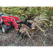 Red compact tractor with black grapple attachment lifting uprooted tree with exposed roots in wooded area