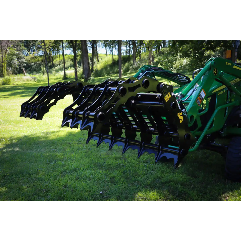 Open black steel grapple attachment mounted on green tractor with visible hydraulic arms on grass outdoors