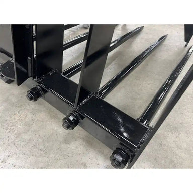 Close-up view of black metal grapple tines with bolts and reinforced welds on concrete floor indoors