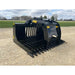Black steel skid steer rock grapple attachment with spaced curved tines and hydraulic cylinders on gravel surface outdoors