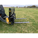 Black skid steer pallet fork attachment with mesh backrest and two straight steel fork tines on grassy field