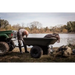 Green Swisher 16 cu ft poly cart hitched to utility vehicle by lakeside with man inspecting tow connection, gallery position 1