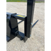 Close-up of black metal skid steer attachment with visible bolt and part of two prongs on gravel surface