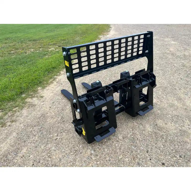 Black steel skid steer pallet fork attachment with perforated vertical backrest and two flat spaced tines on gravel surface