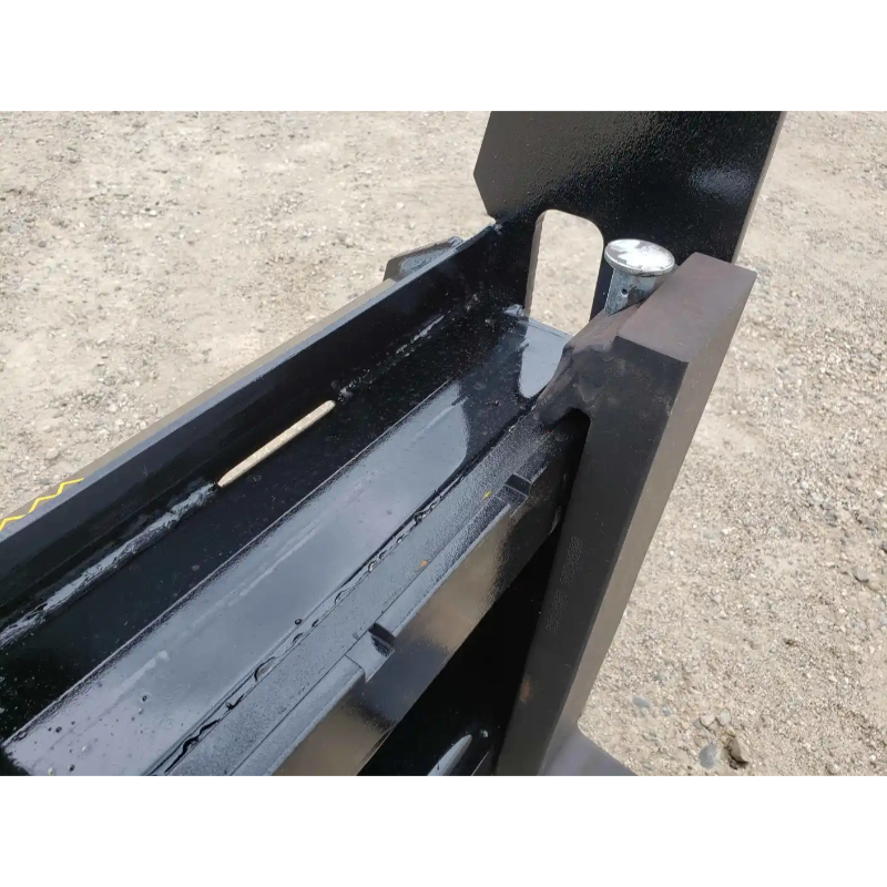 Close-up of black painted steel forklift attachment mounting plate with locking pin and channel on gravel surface