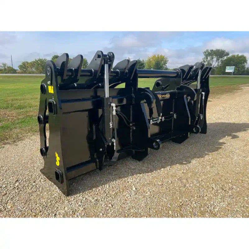 Black steel clam grapple attachment with hydraulic cylinders and reinforced mounting brackets on gravel outdoors