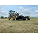 Yellow Deere loader with large black mechanical claw grapple attachment lowered over dry grass field under cloudy sky