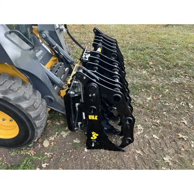 Right-side view of black steel clam grapple attachment mounted on yellow skid steer loader on dirt ground outdoors
