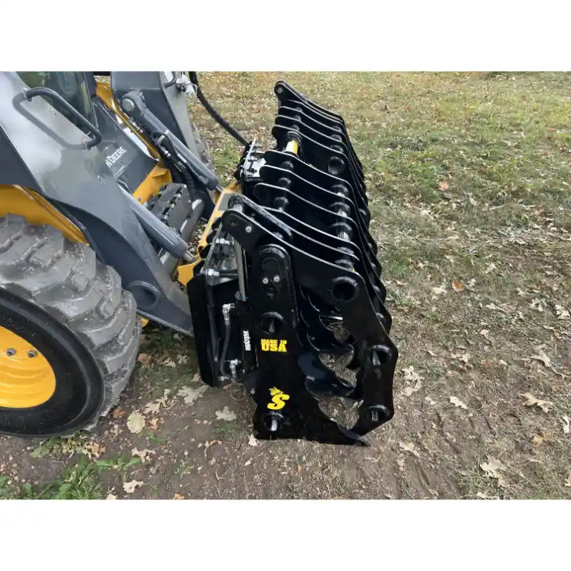 Right-side view of black steel clam grapple attachment mounted on yellow skid steer loader on dirt ground outdoors