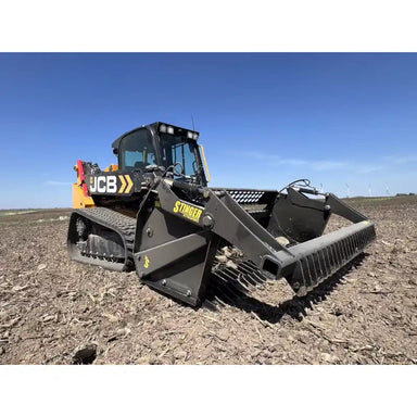 Front-left angled view of black skid steer with rock reel attachment on dry soil under clear blue sky