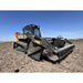 Front-left angled view of black skid steer with rock reel attachment on dry soil under clear blue sky