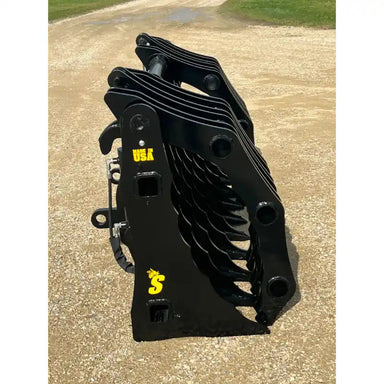 Black steel clam grapple attachment with multiple curved tines standing upright on gravel surface outdoors